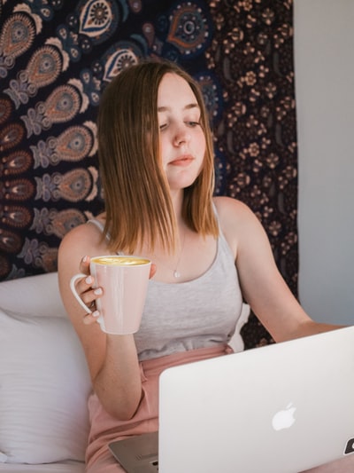 坐在床上拿着马克杯用MacBook的女人